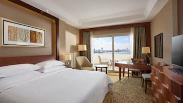 Habitación de hotel con una cama grande, un escritorio, una silla, un televisor y vistas a la ciudad desde la ventana.