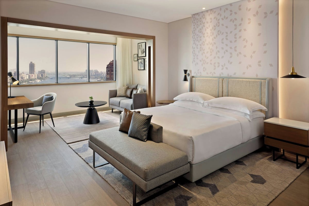 Una habitación de hotel moderna con una cama grande, un sofá, un área de comedor y vistas a la ciudad.
