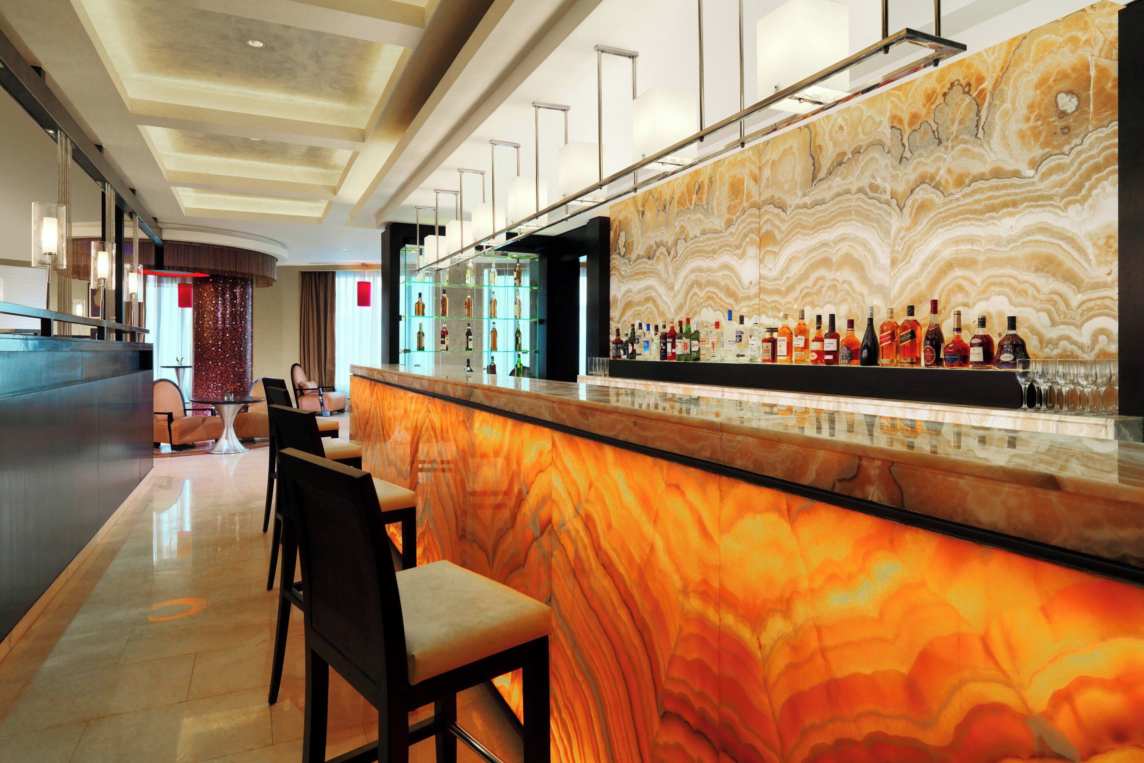 A modern bar area with a marble countertop, bar stools, and a variety of liquor bottles.