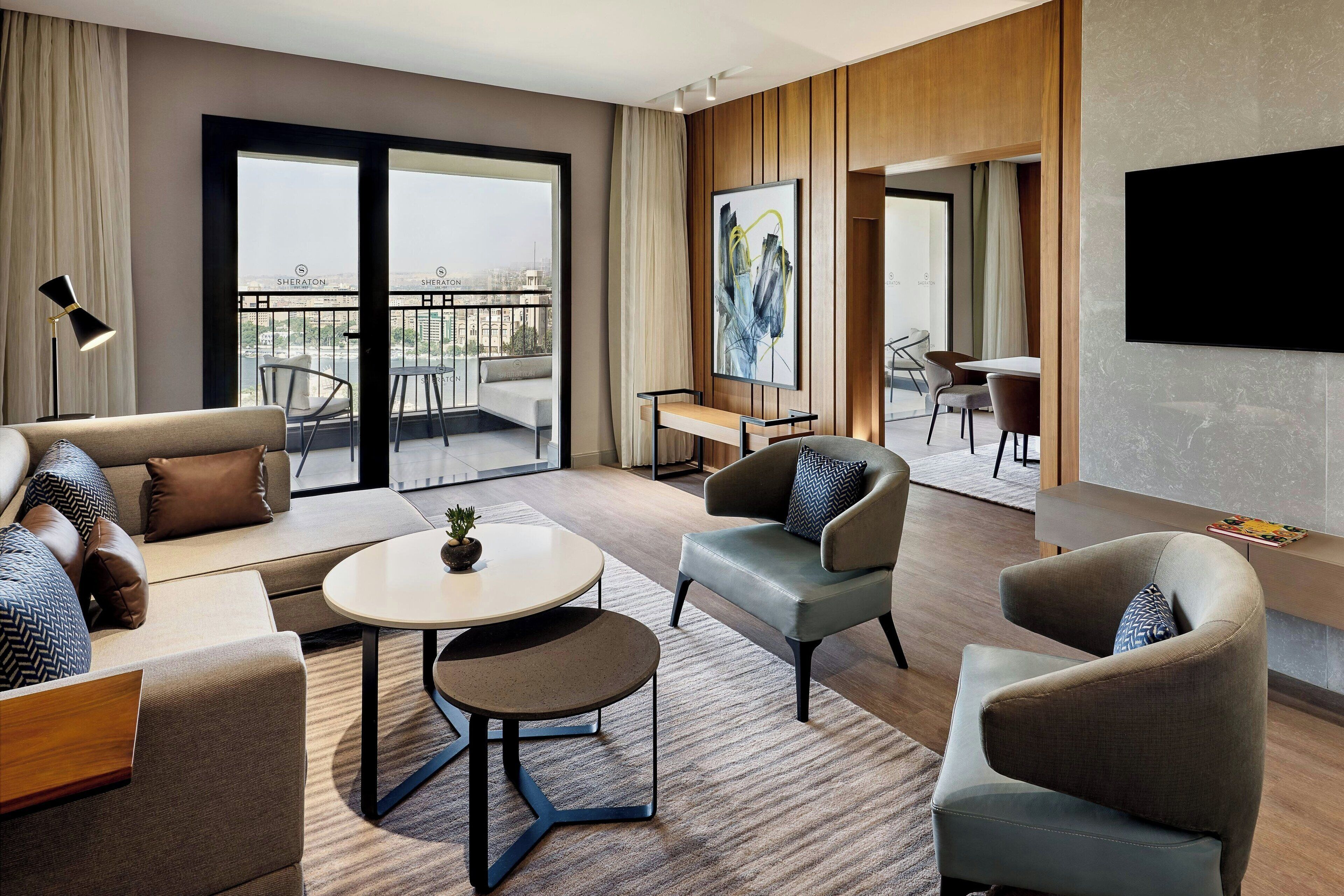 Ein modernes Hotelzimmer mit einer Couch, Sesseln, einem kleinen Tisch und einem Balkon mit Blick.