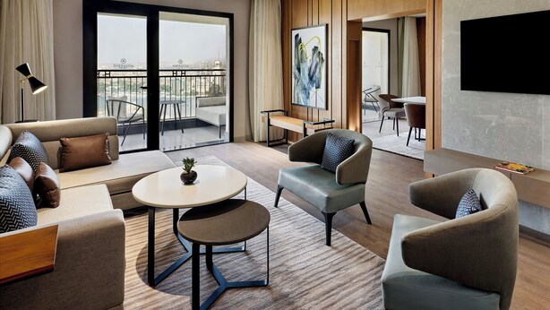 A modern hotel room with a sofa, armchairs, a small table, and a balcony with a view. - Sheraton Cairo Hotel & Casino (Giza)