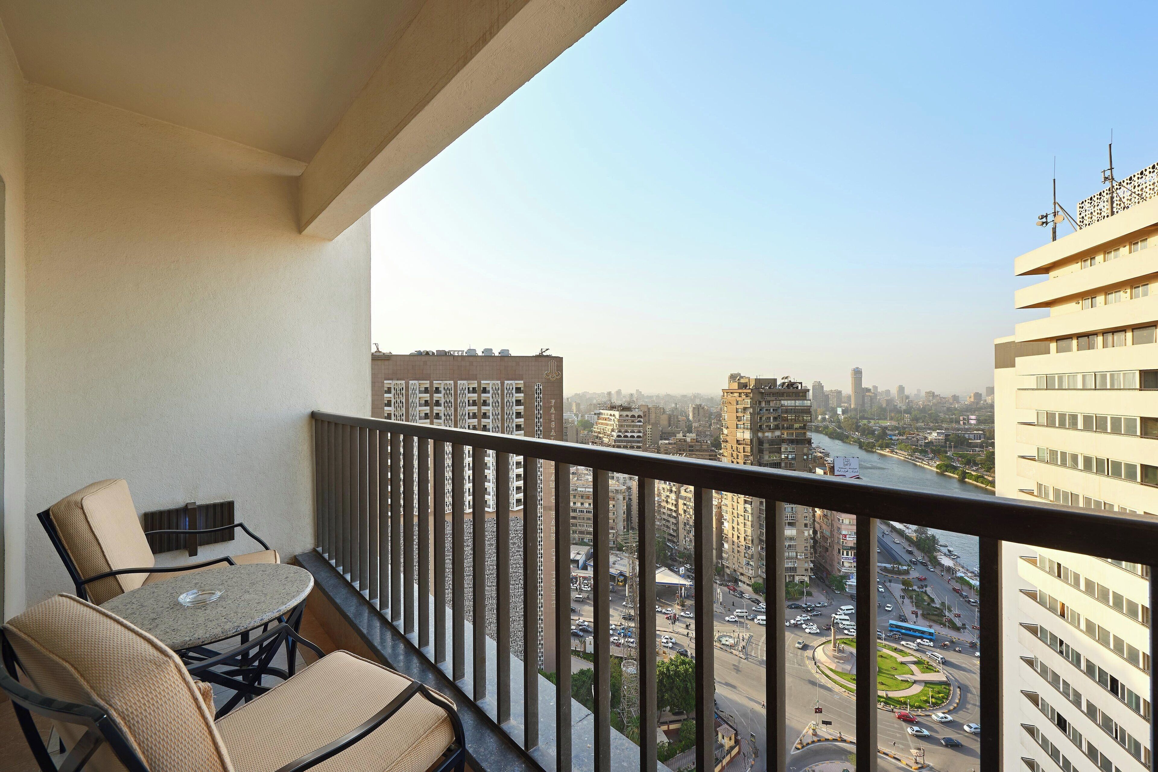 A balcony with a table and chairs, overlooking a cityscape with tall buildings and a river.