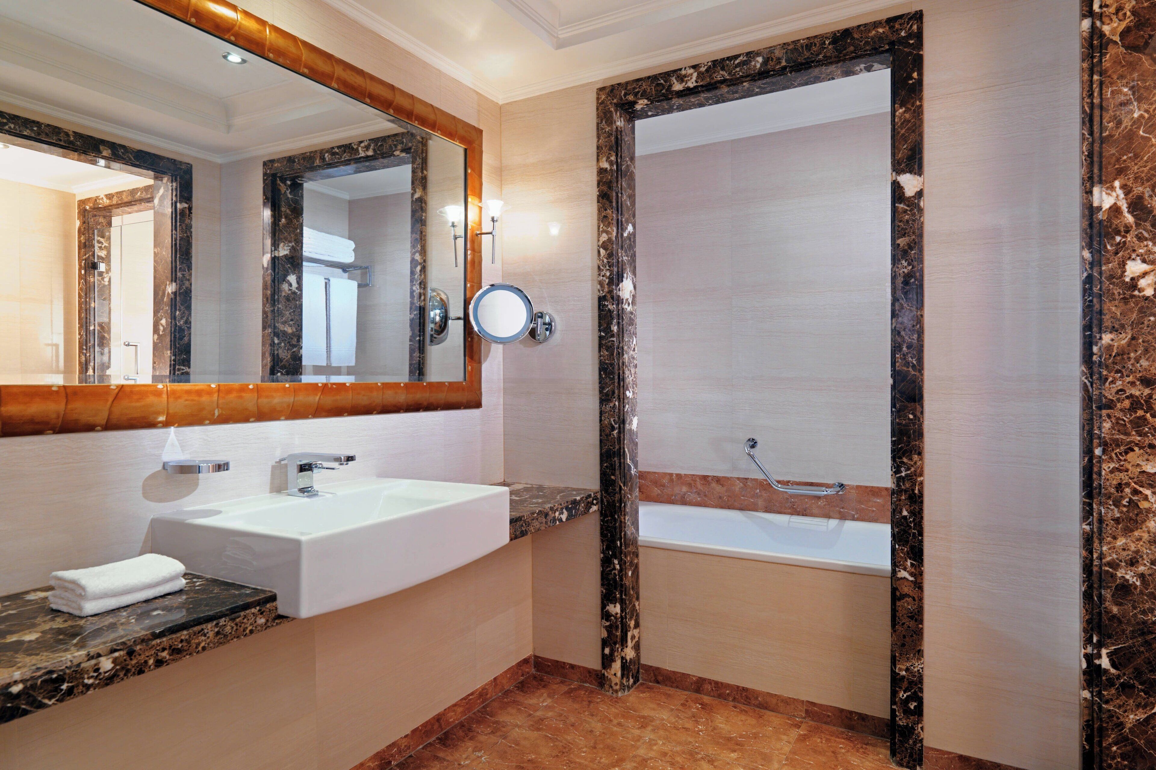 A bathroom with a marble vanity, a large mirror, a bathtub, and a shower.