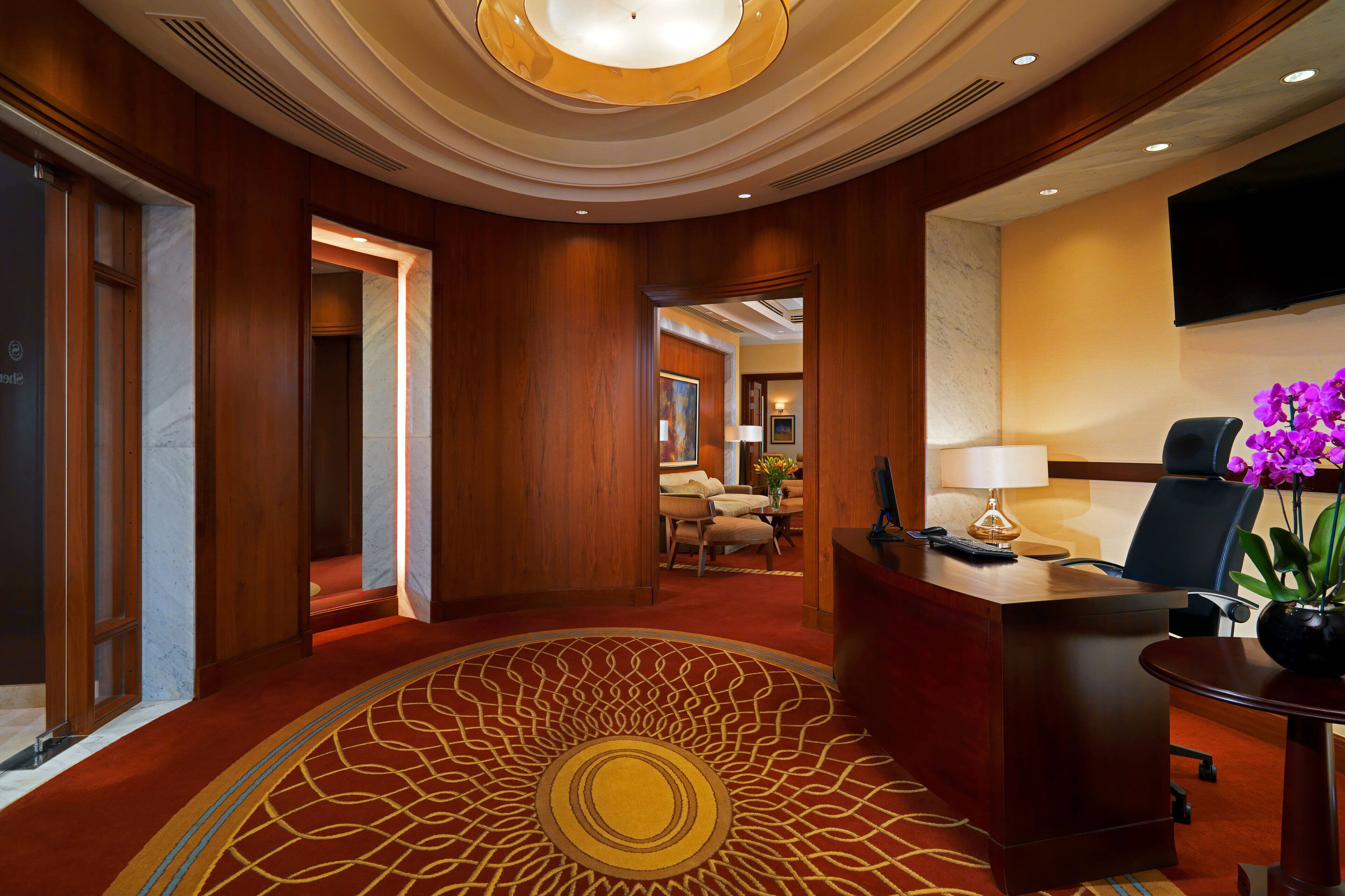 A hotel lobby with a reception desk, a seating area with chairs, and a large decorative carpet.