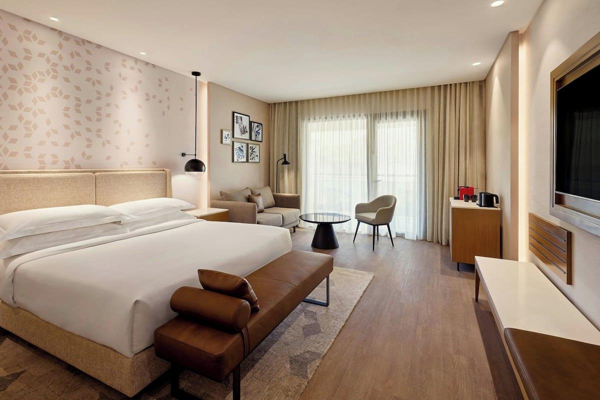 Una habitación de hotel moderna con una cama grande, un sofá, una mesita y un televisor.