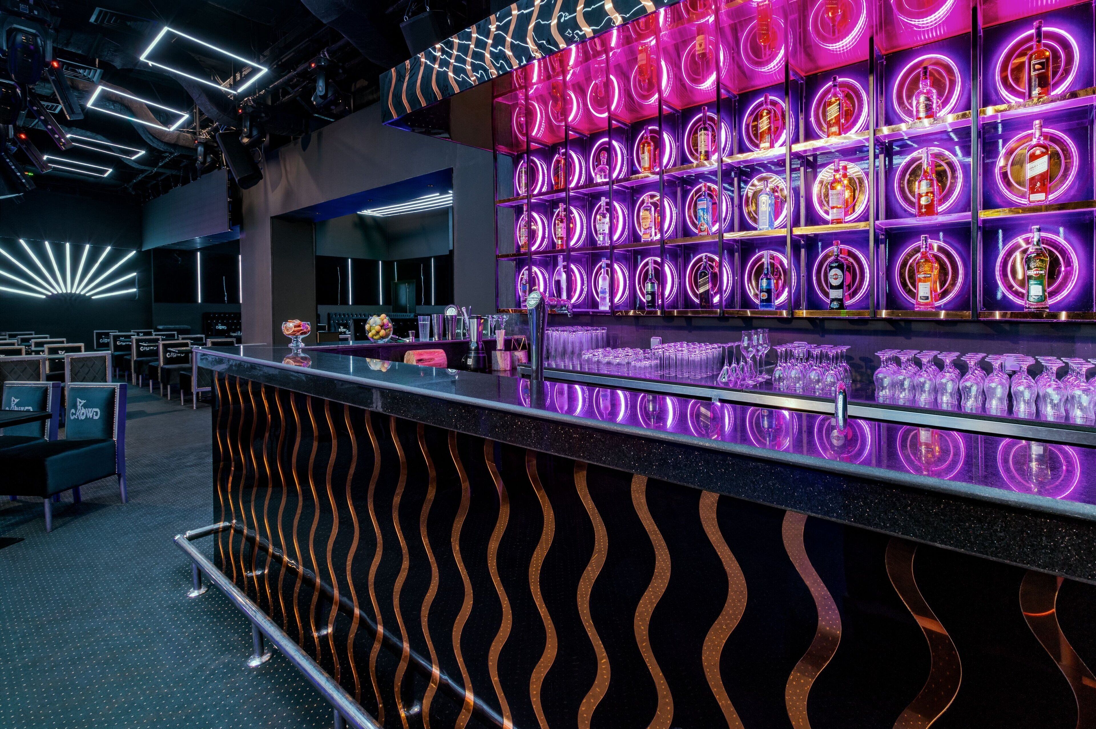 A bar area with a neon-lit wall of liquor bottles, a counter with glasses, and a seating area with a 'CROWD' sign.