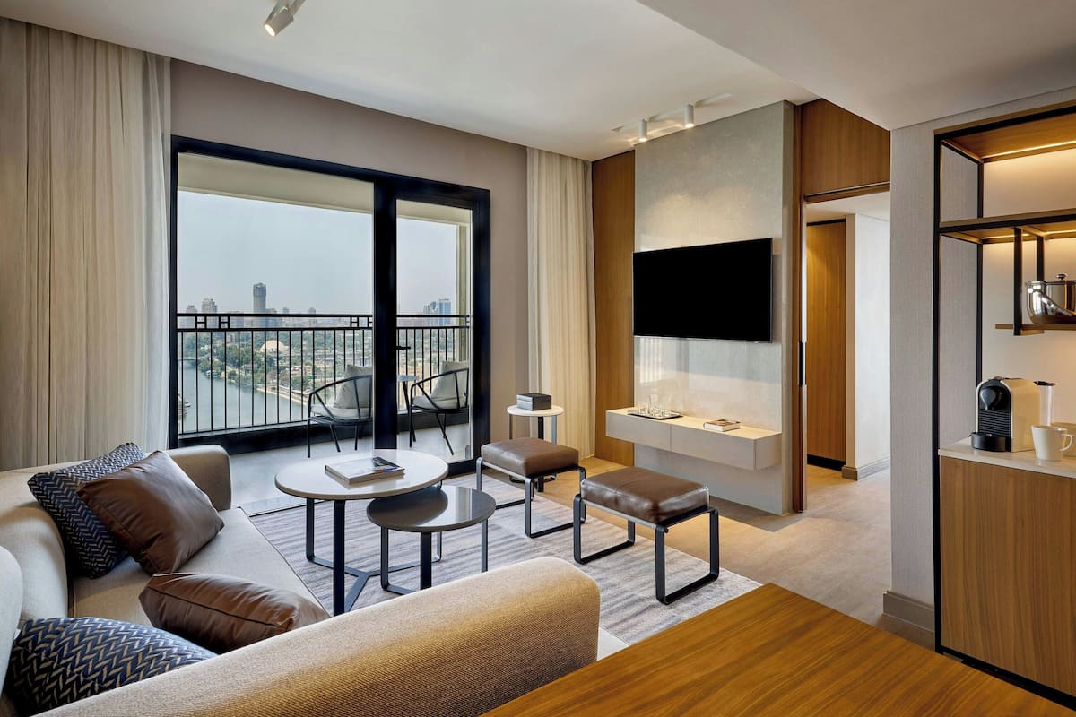 Una habitación de hotel moderna con un balcón grande, un sofá, una mesa de centro y un televisor montado en la pared.