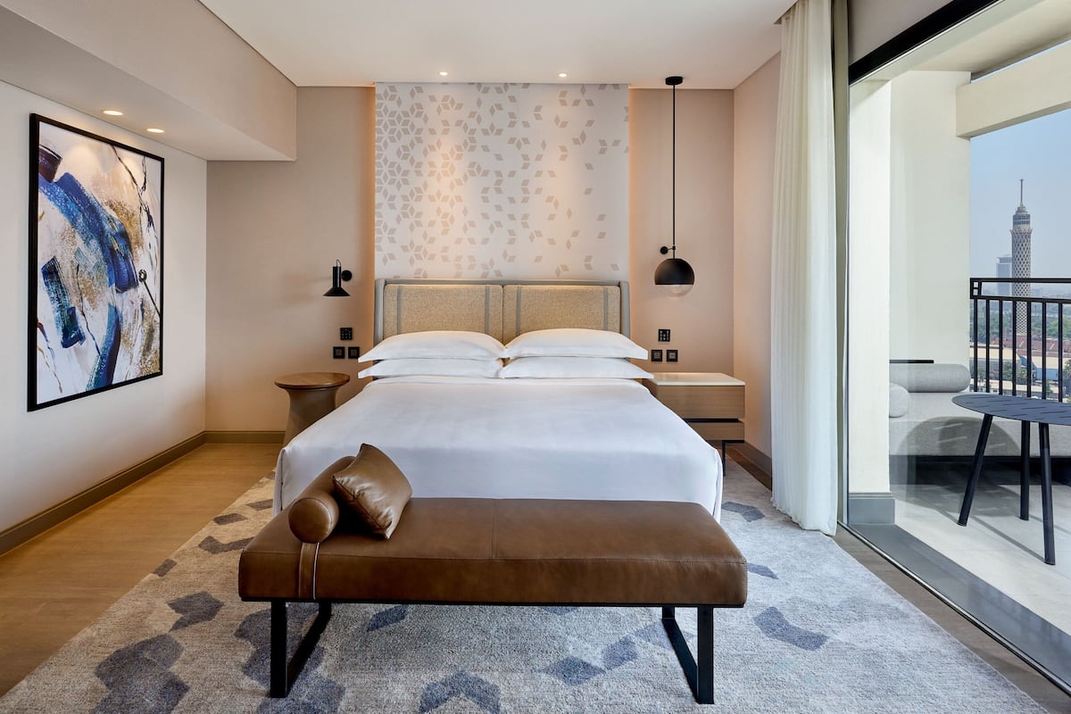 Habitación de hotel con una cama grande, un banco, vistas a un paisaje urbano y una decoración moderna.