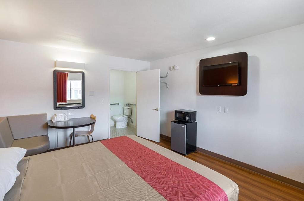 A hotel room with a bed, a desk, a microwave, a TV, and a bathroom visible through an open door.