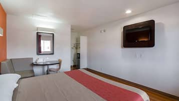 Ein Hotelzimmer mit Bett, Schreibtisch, Stuhl, Wandfernseher und Spiegel über dem Schreibtisch.