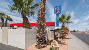 A motel with a prominent '6' sign, palm trees, and a red building in the background.