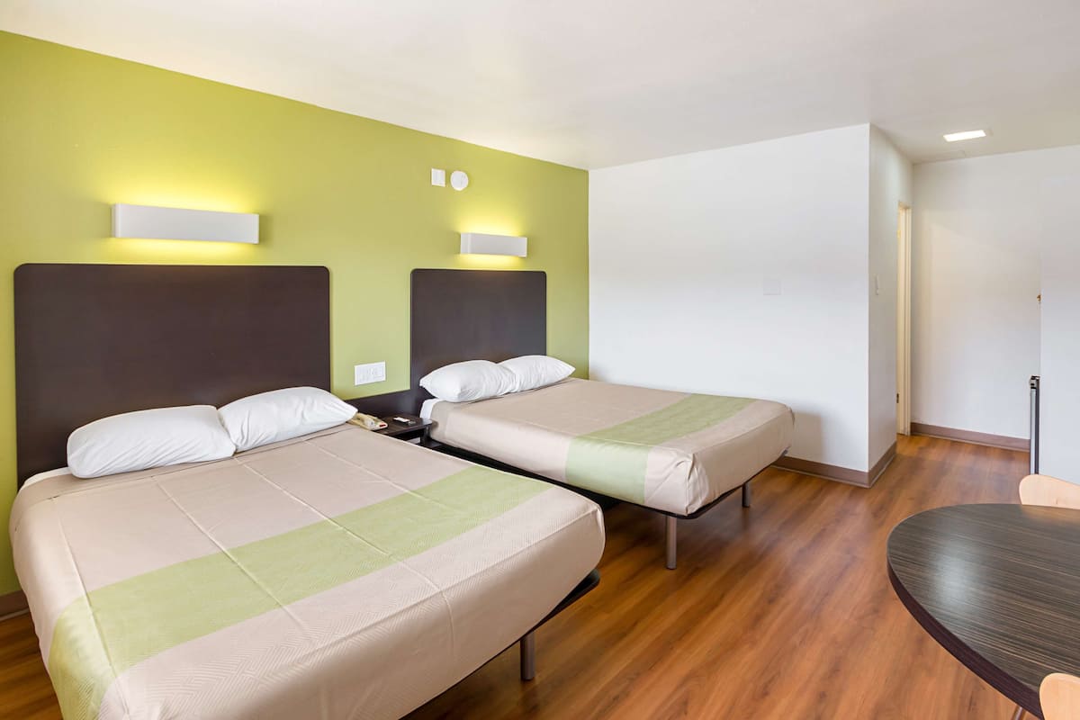 Una camera d'albergo con due letti, pavimento in legno e un tavolino.