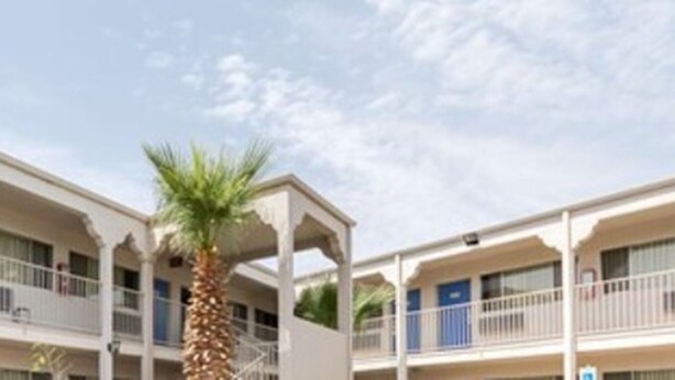 A multi-story hotel with balconies and a palm tree.