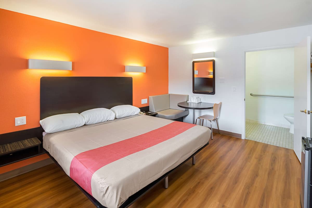 Una camera d'albergo con un letto grande, un tavolino, una sedia, uno specchio e la porta del bagno.