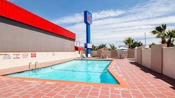 A swimming pool with a red and blue sign, a brick patio, and a clear sky.