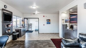 A hotel lobby with a reception desk, a TV mounted on the wall, a trash bin, a black leather sofa, and a red rug. - Motel 6 Wisconsin Rapids, WI (Wisconsin Rapids)