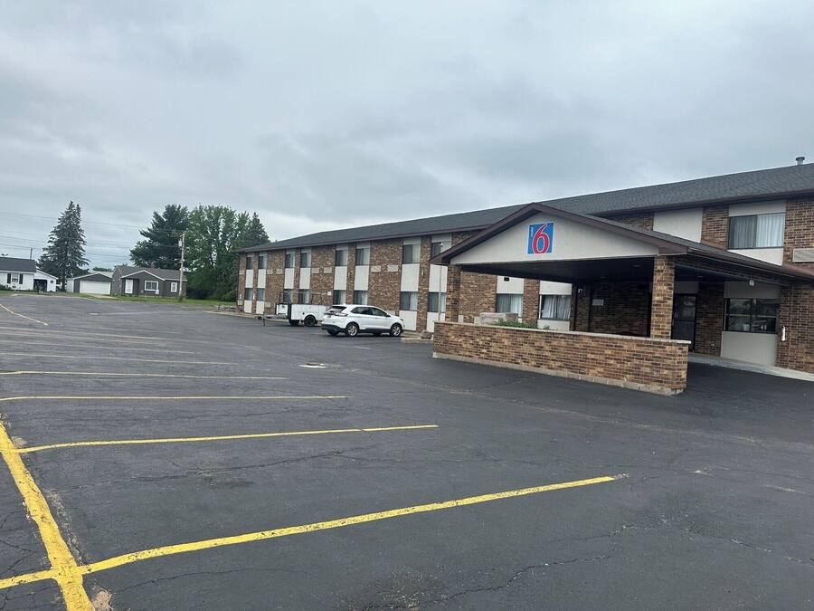A motel with a parking lot and a white car parked in front.