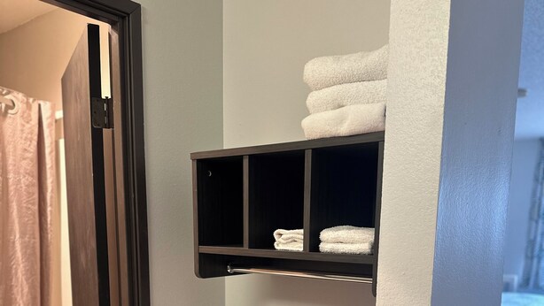 A bathroom with a shower curtain, a towel rack with folded towels, and a tissue box on a shelf. - Motel 6 Wisconsin Rapids, WI (Wisconsin Rapids)