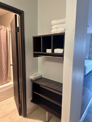 A bathroom with a shower curtain, a towel rack with folded towels, and a tissue box on a shelf. - Motel 6 Wisconsin Rapids, WI (Wisconsin Rapids)