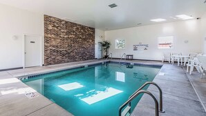 An indoor swimming pool with a brick wall, white walls, and a seating area with white chairs. - Motel 6 Wisconsin Rapids, WI (Wisconsin Rapids)
