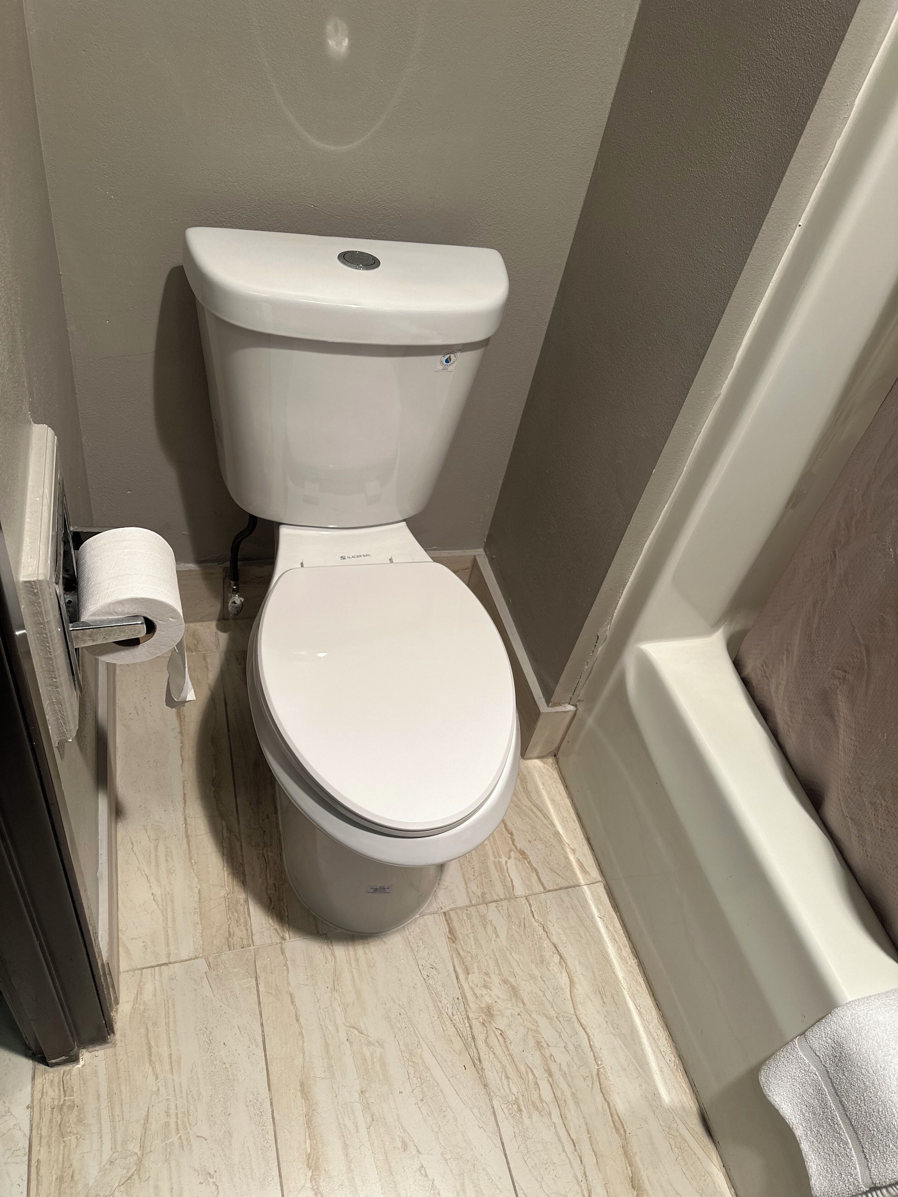 Un inodoro con tapa y tanque blancos, un rollo de papel higiénico en la pared, y un suelo de mármol.