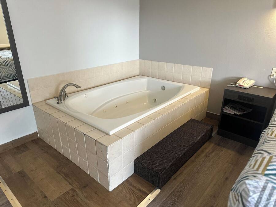 Un bagno moderno con una vasca freestanding, un comodino con un telefono e documenti, e un pavimento in legno.