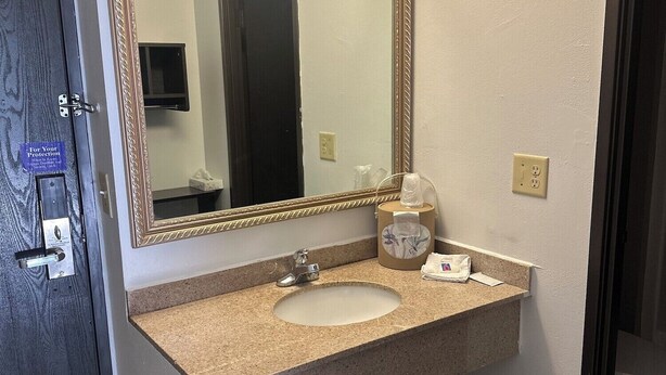 Une salle de bain avec un grand miroir, un lavabo, une poubelle et un distributeur de serviettes.