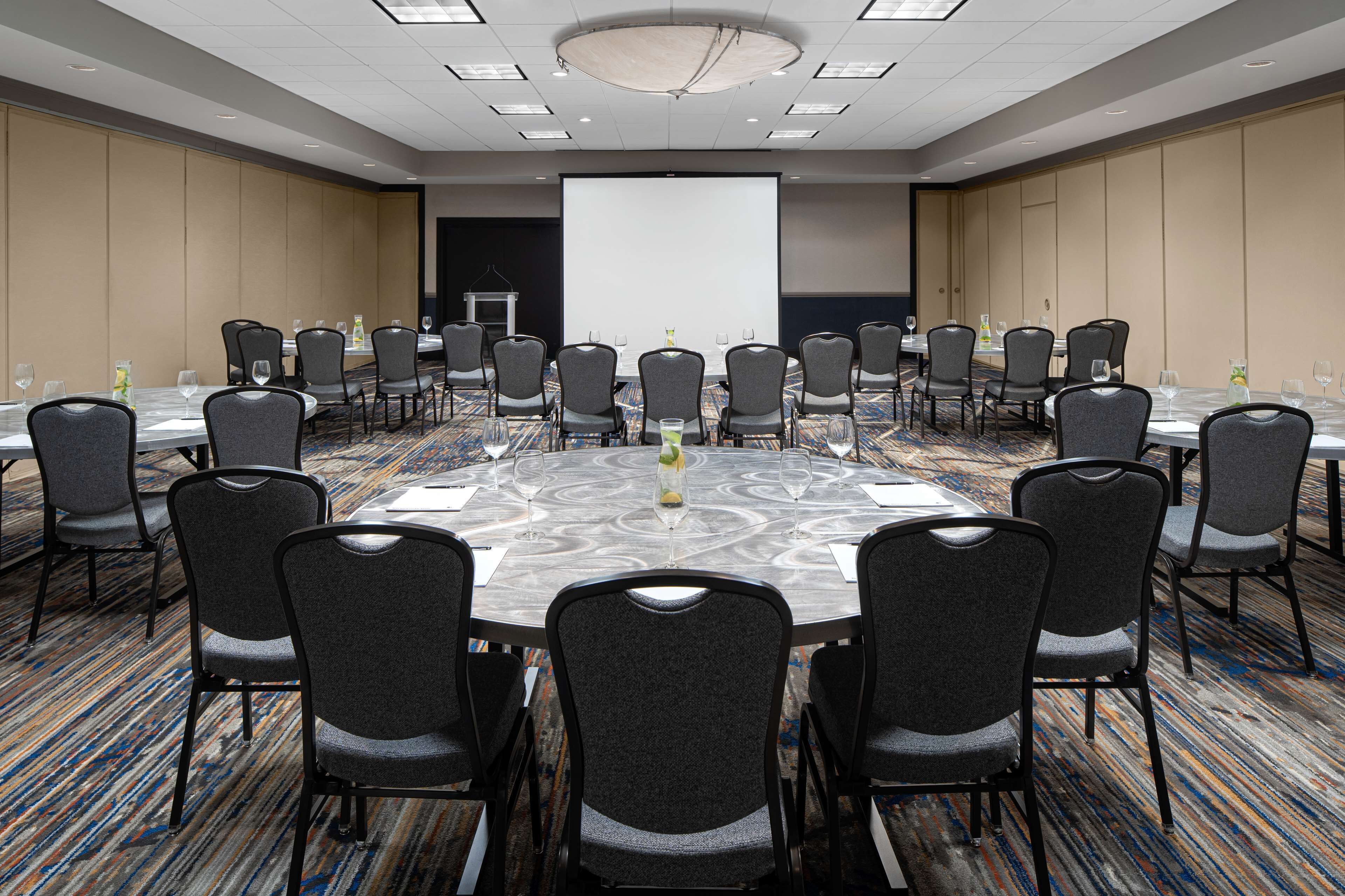 A conference room with a large screen, round tables, and chairs arranged for meetings.