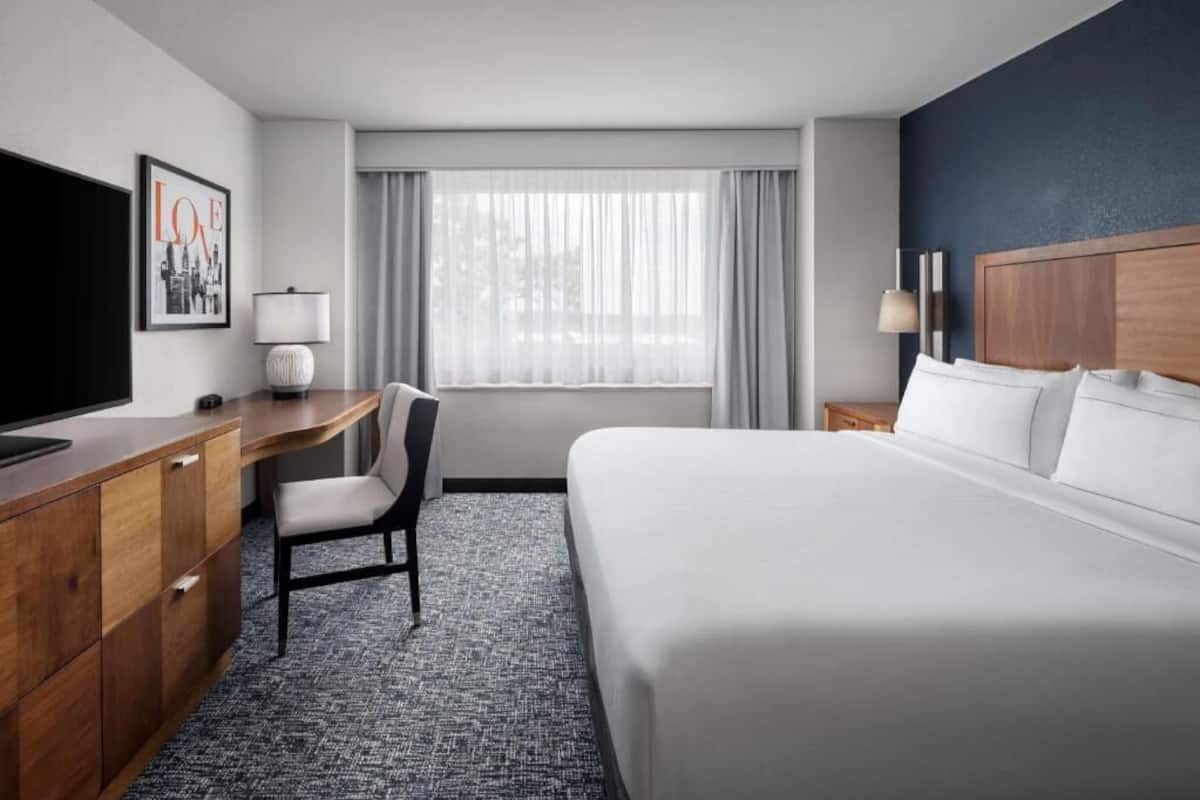 A hotel room with a bed, desk, chair, TV, and a window with curtains.
