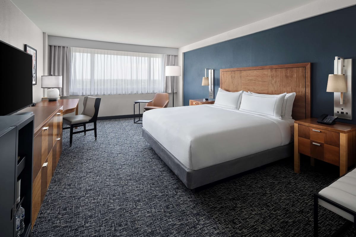 A hotel room with a large bed, a desk with a chair, a TV, and a window with curtains.