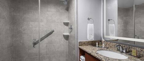 A modern bathroom with a glass-enclosed shower, a large sink with a granite countertop, and a mirror above the sink.