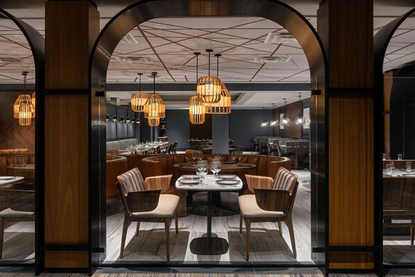 A modern dining area with a central round table, wooden chairs, and hanging pendant lights.
