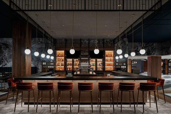 A bar area with a marble wall, wooden bar counter, and multiple hanging light fixtures.