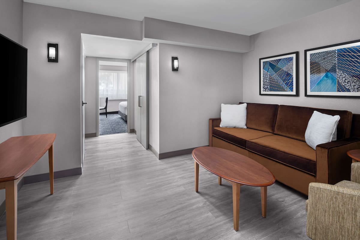 A modern hotel room with a brown sofa, a wooden coffee table, and a flat-screen TV.