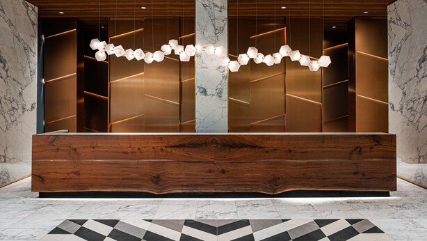 A reception area with a wooden reception desk, marble walls, and a geometric patterned floor. - The Alloy King of Prussia - a DoubleTree by Hilton (King of Prussia)