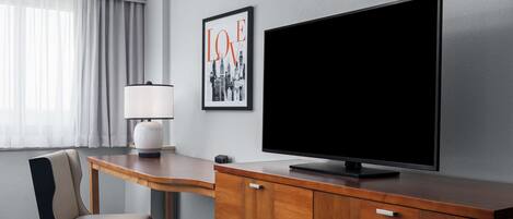 A hotel room with a wooden desk, a television, a chair, and a framed picture on the wall.