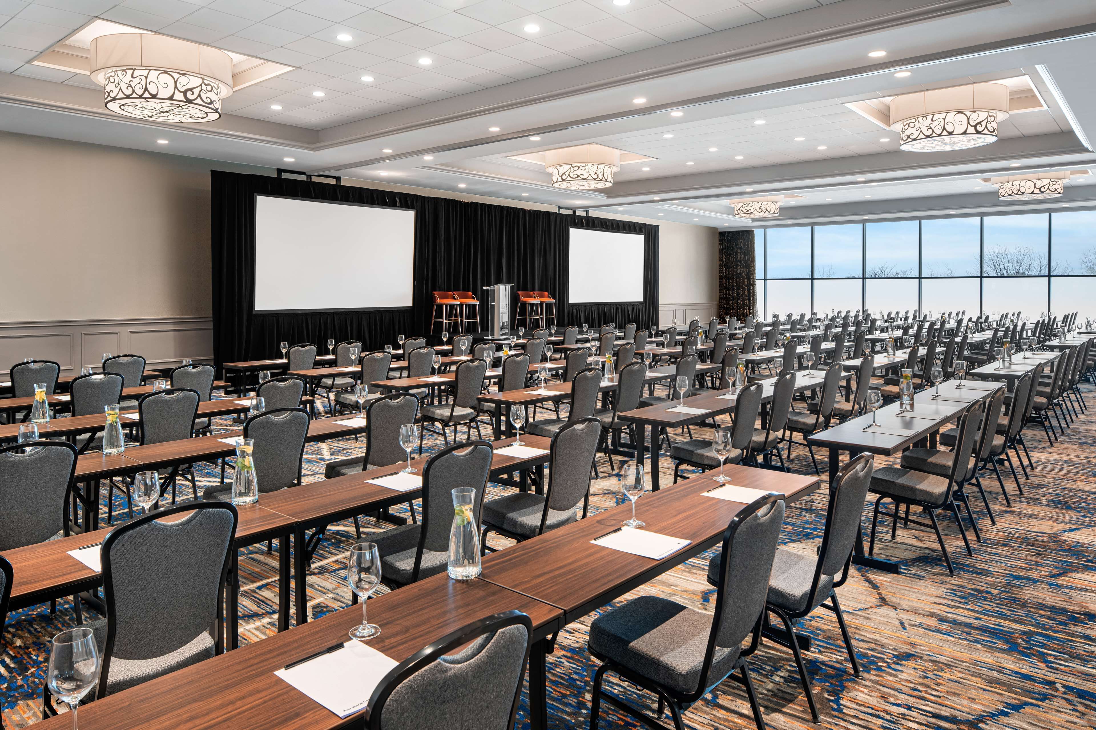 A conference room with rows of tables, chairs, and a large screen.