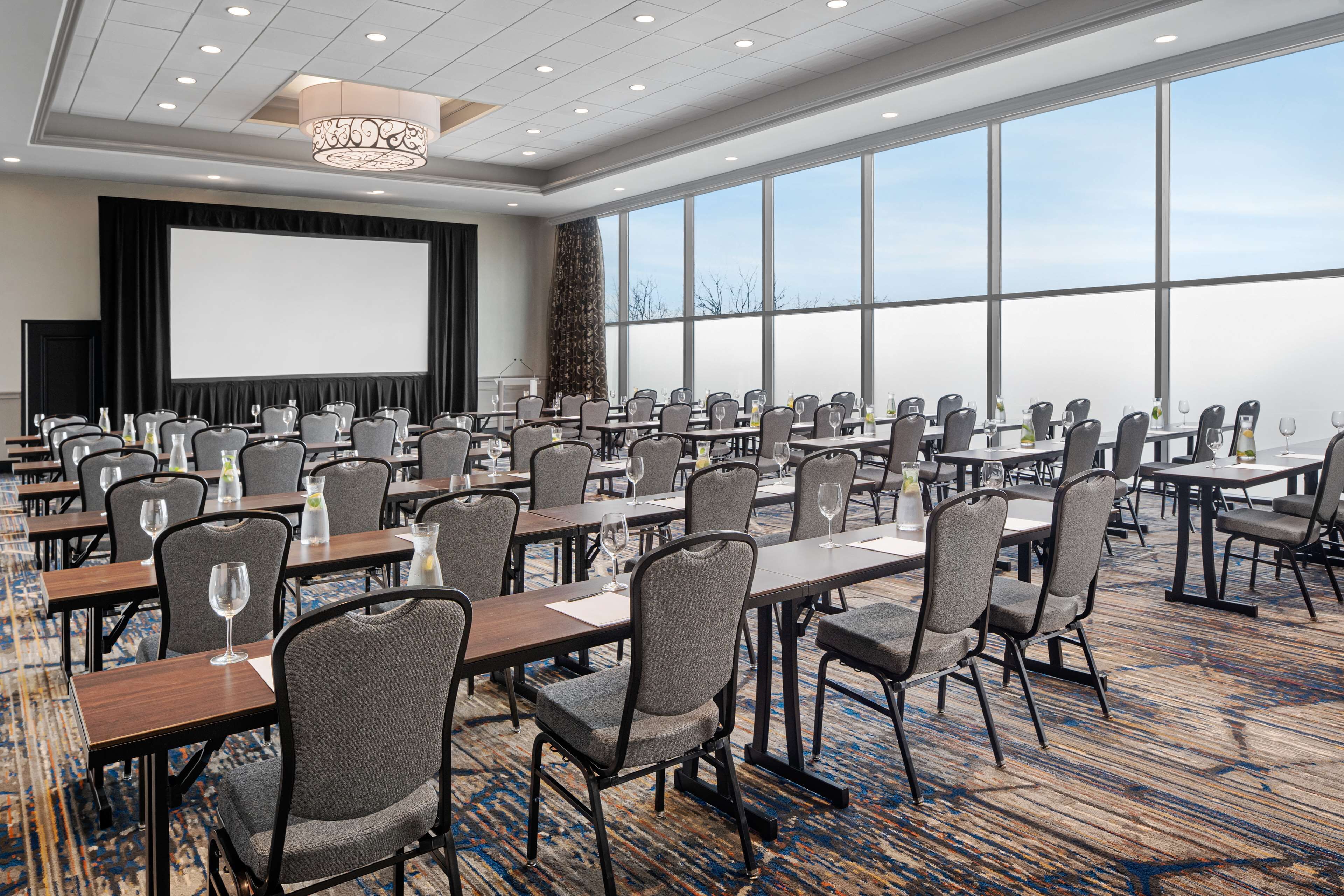 A conference room with a large screen, multiple tables with chairs, and a carpeted floor.