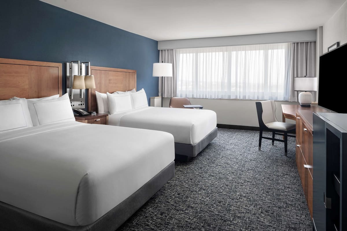 A hotel room with two beds, a desk, a chair, and a TV.