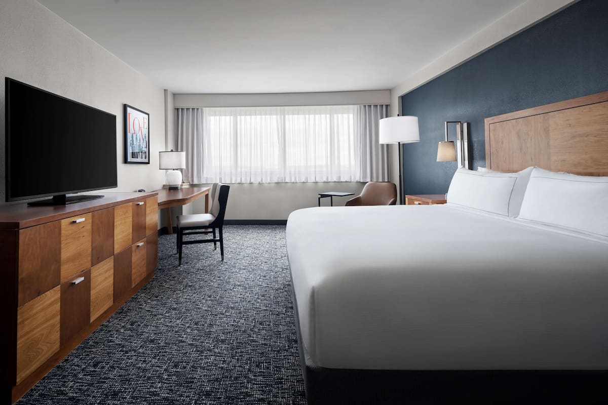 A hotel room with a large bed, a desk with a chair, a television, and a window with curtains.