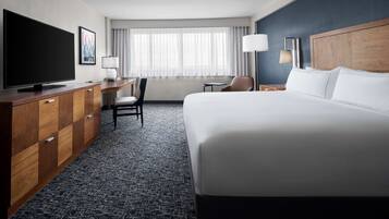 A hotel room with a large bed, a desk with a chair, a television, and a window with curtains.