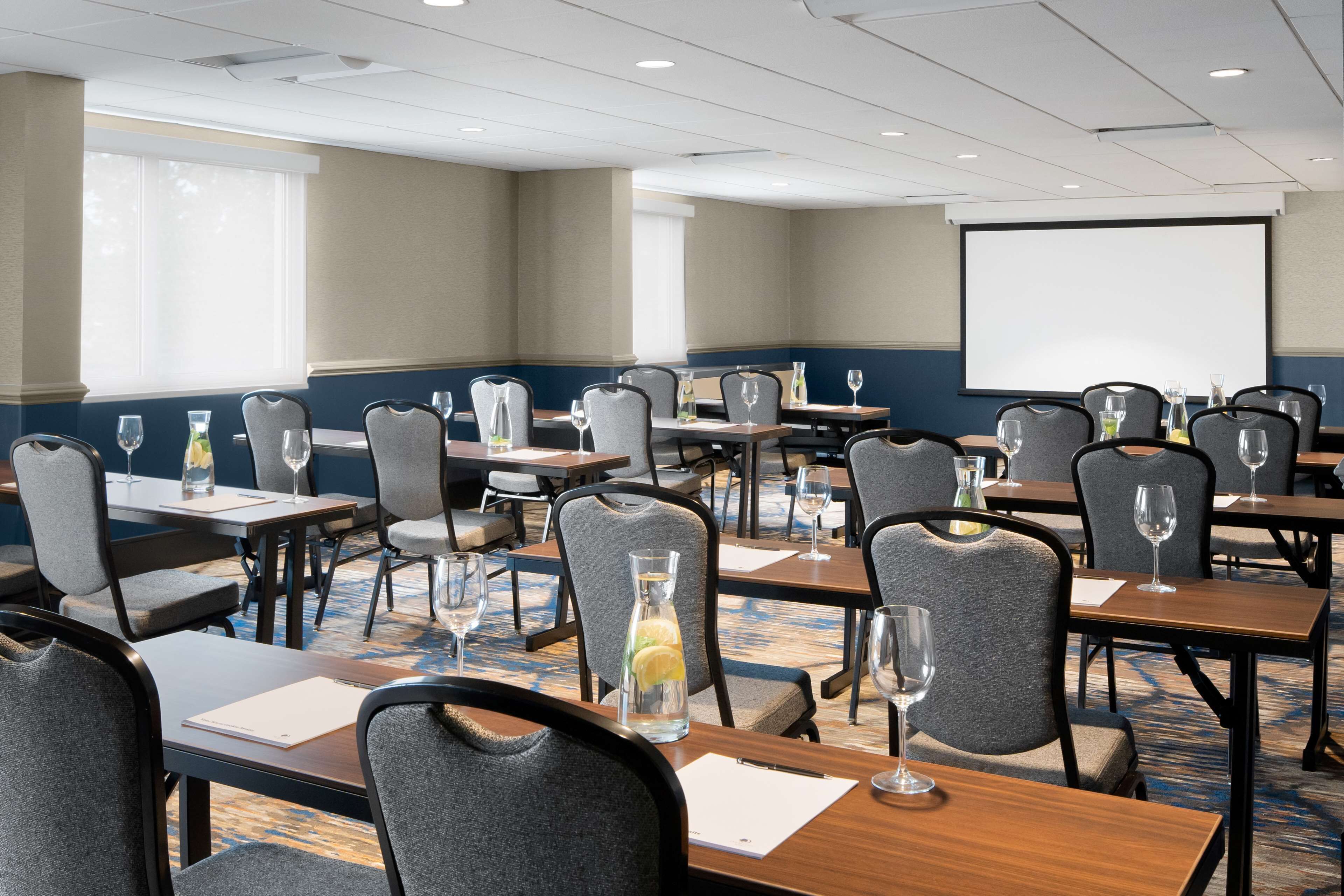 A conference room with tables, chairs, a projector screen, and a carpeted floor.
