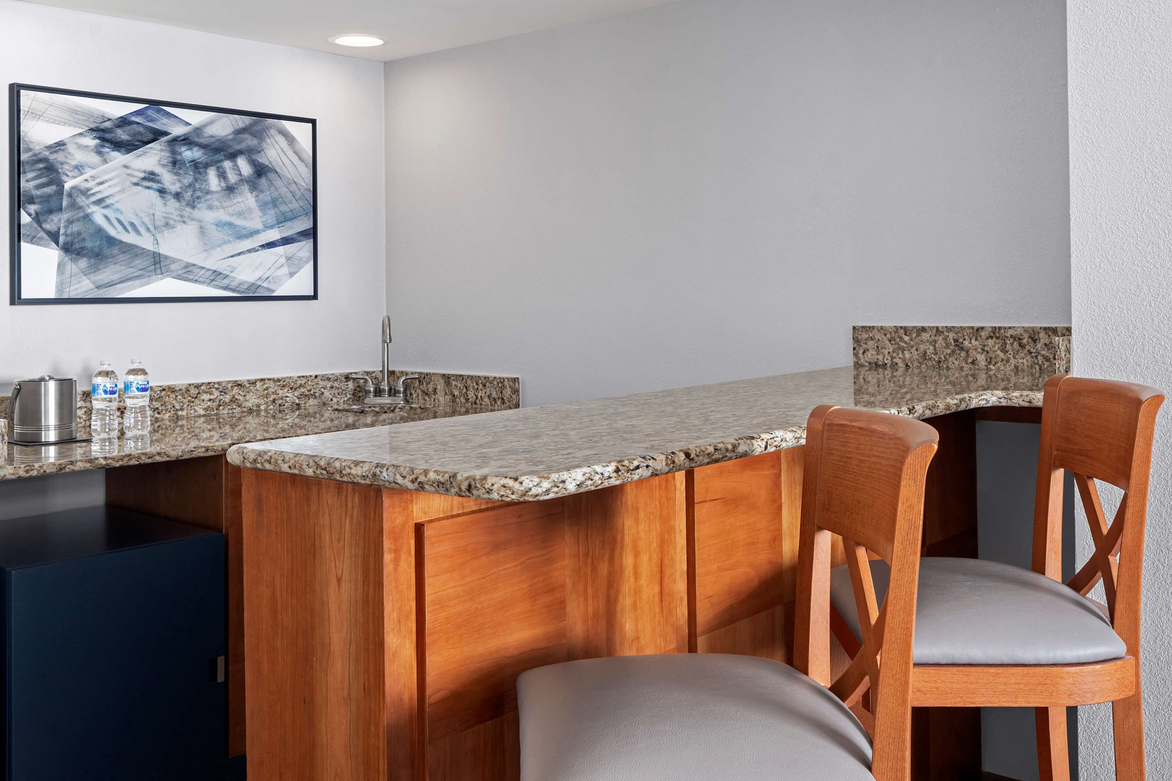 A modern kitchen with granite countertops, wooden bar stools, and a stainless steel sink.