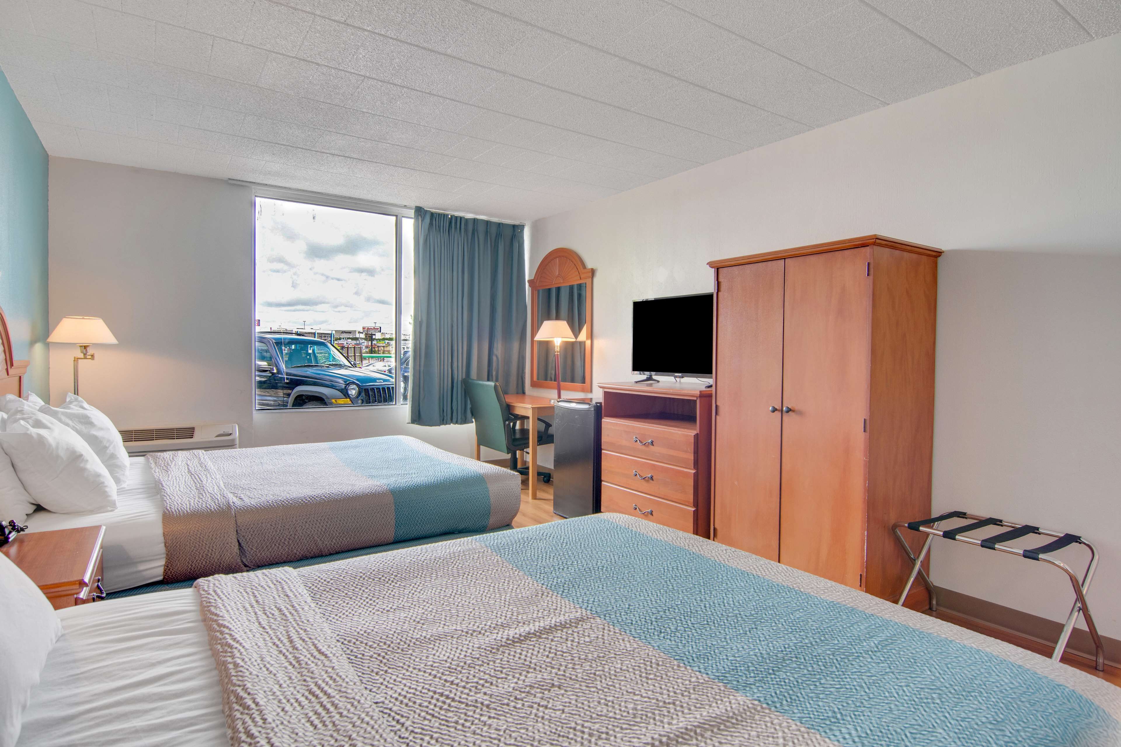 A hotel room with two beds, a desk, a TV, a wardrobe, and a window with a view of the outside.