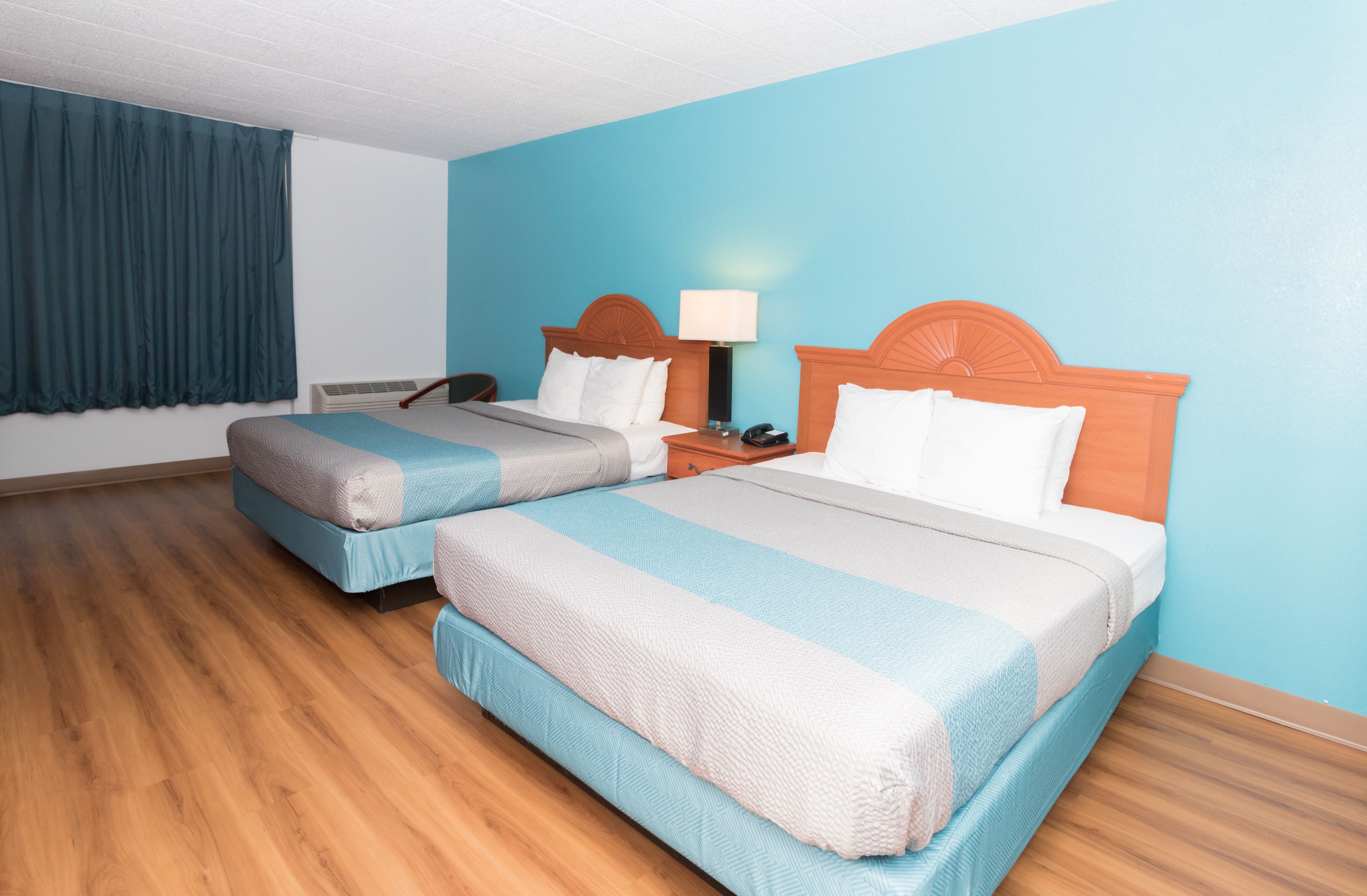 A hotel room with two beds, a nightstand, a lamp, and a telephone.