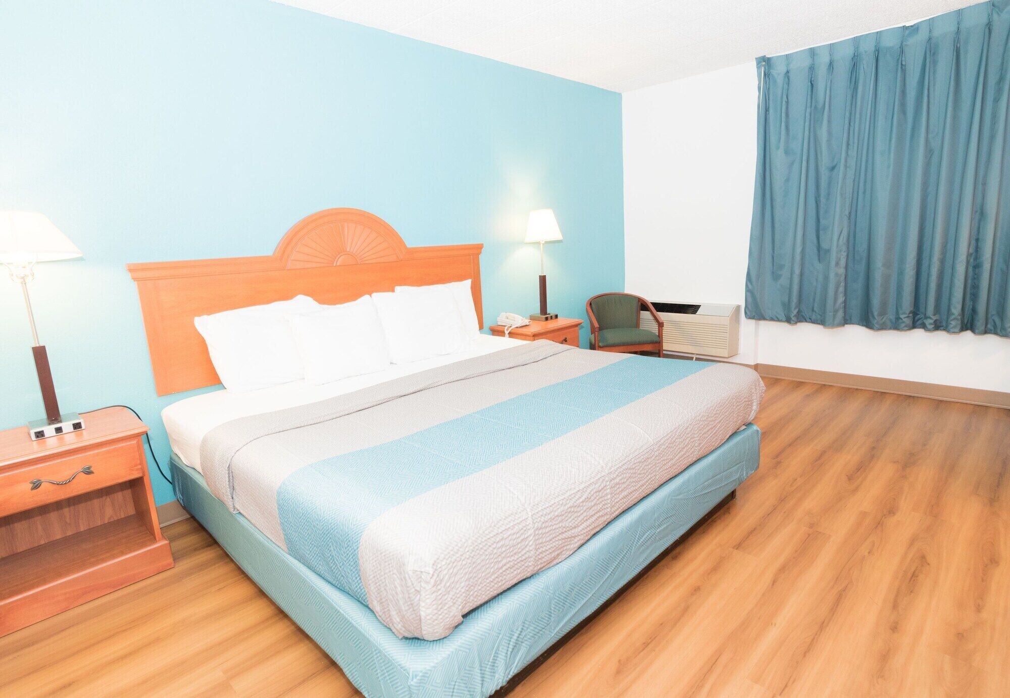 Een hotelkamer met een bed, nachtkastje, stoel en raam met gordijnen.