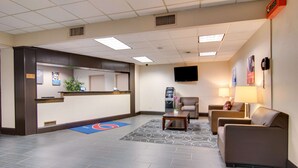 A hotel lobby with a reception desk, seating area, and a flat-screen TV mounted on the wall.