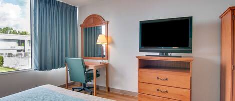 Una habitación de hotel con una cama, un escritorio con una silla, un televisor y un aparador de madera.