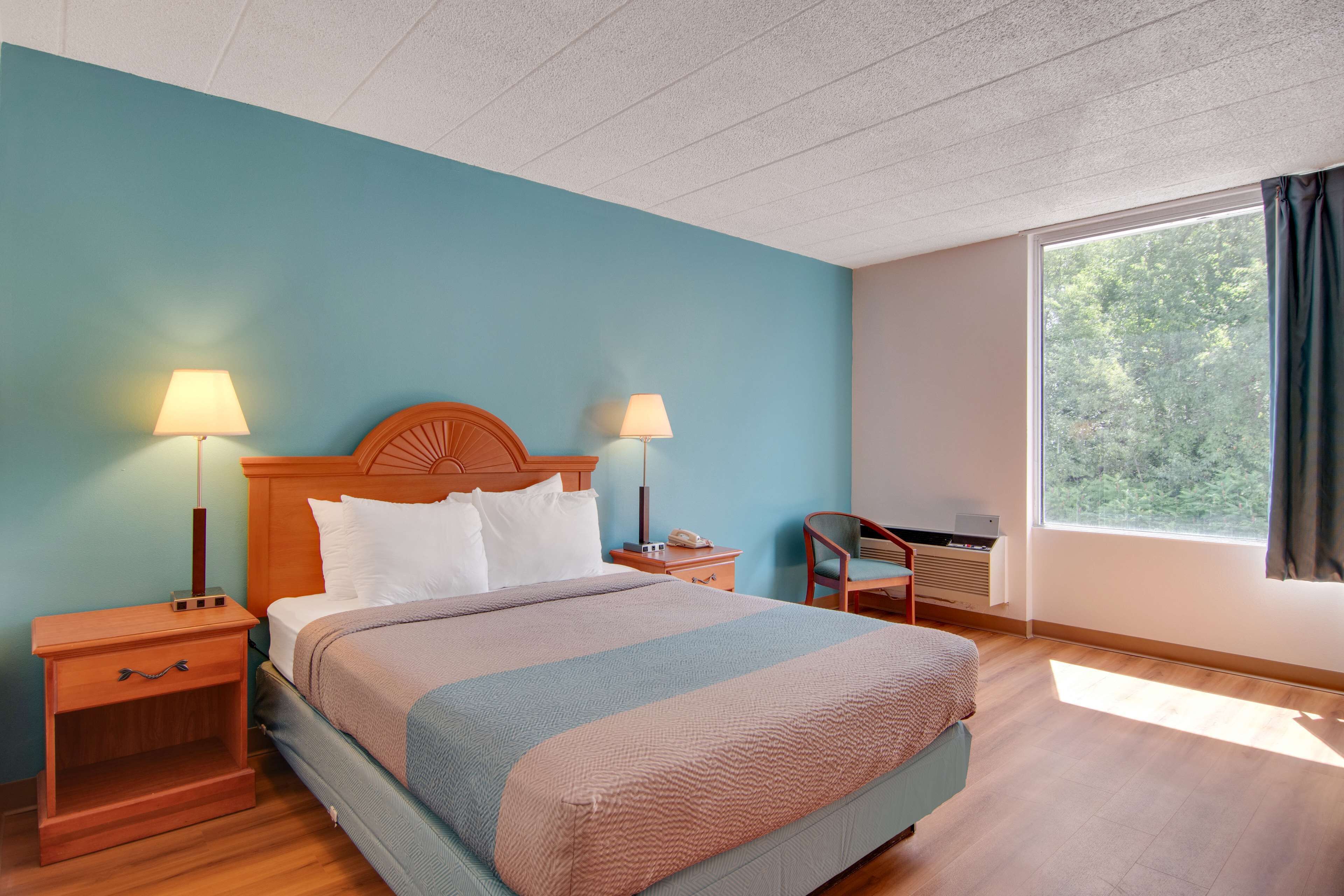 Un cuarto de hotel ordenado con una cama, dos lámparas de noche, un sillón y un ventanal grande.