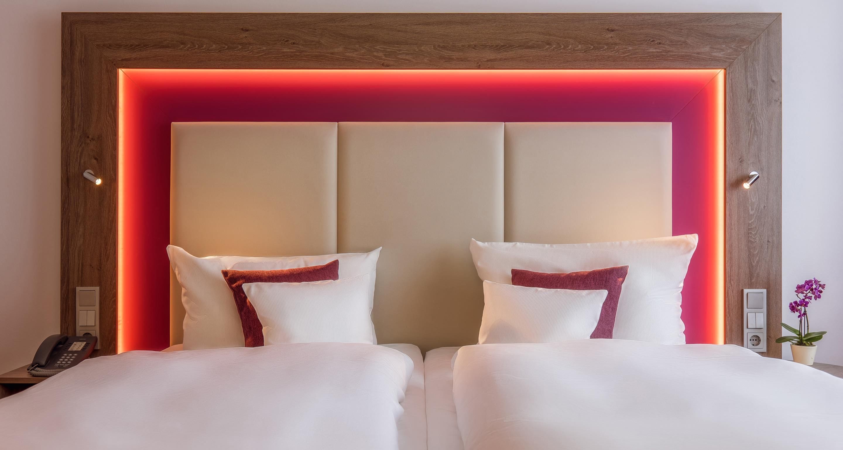 Habitación de hotel con una cama grande, dos almohadas, un cabecero de madera y una tira de luz roja.